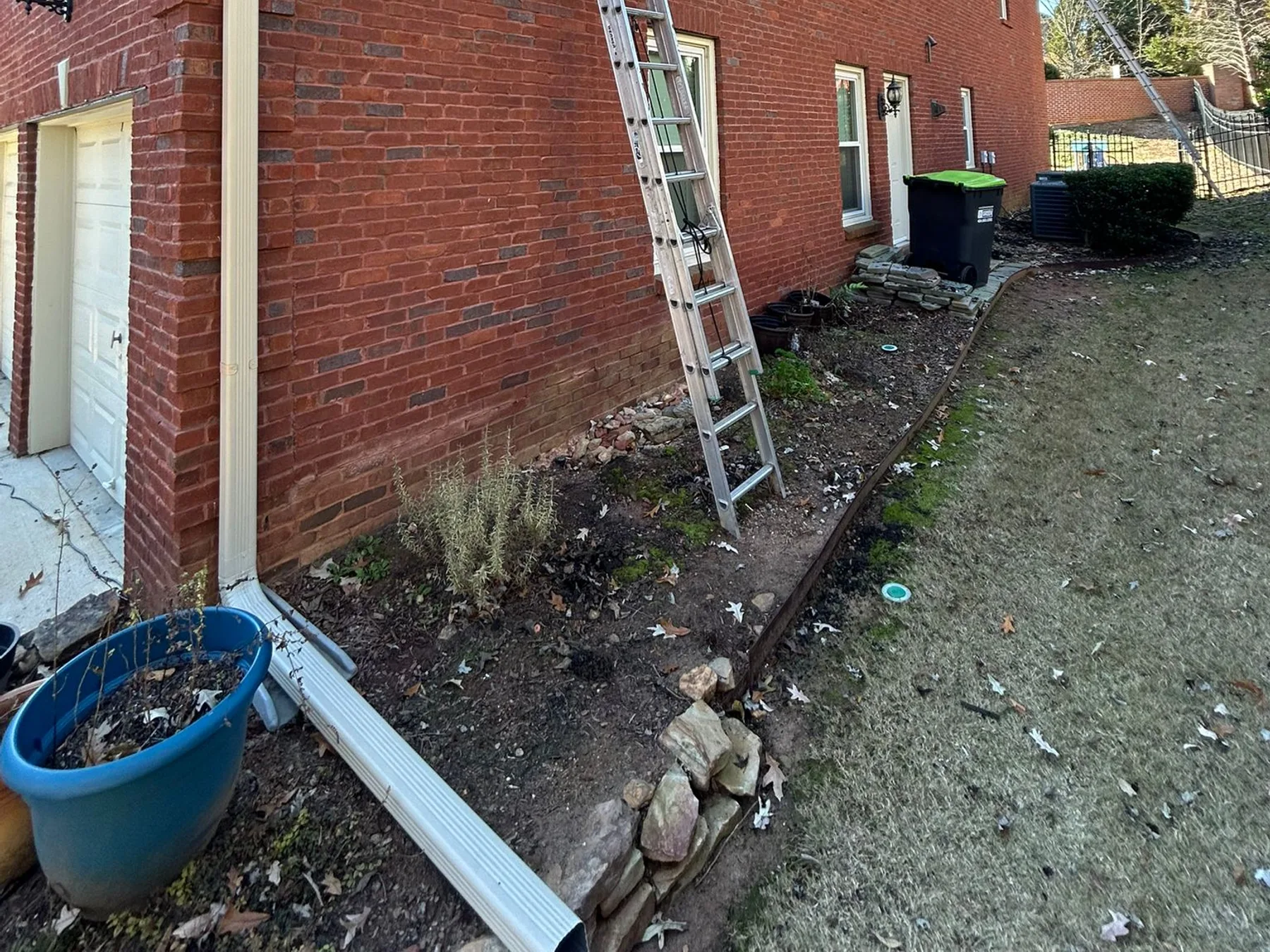 AJ Gutters LLC technician on a ladder installing gutters on a two-story brick home
