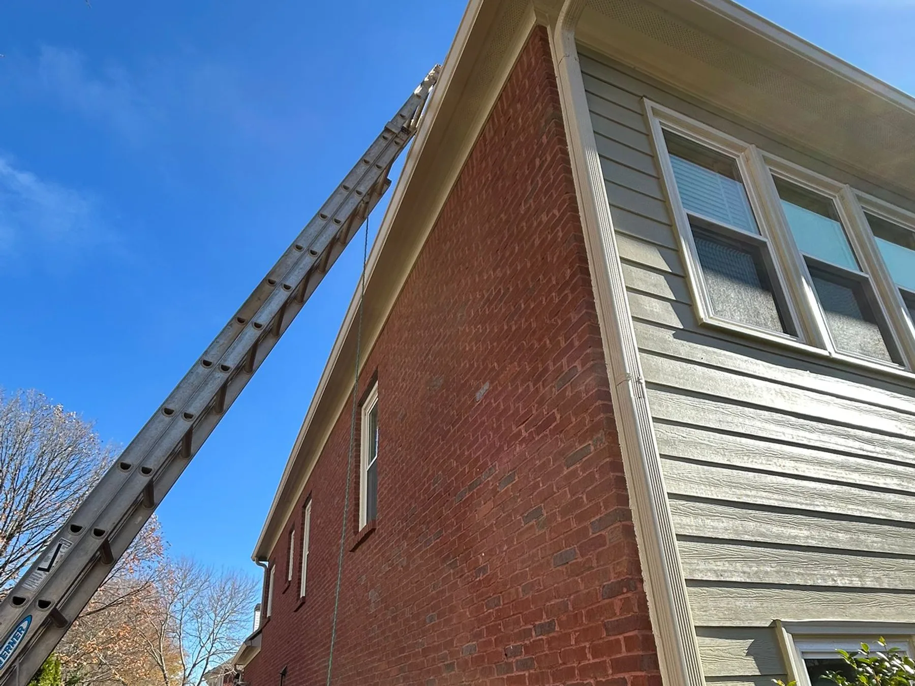 Bucket truck ladder extended to a brick home gable for gutter work